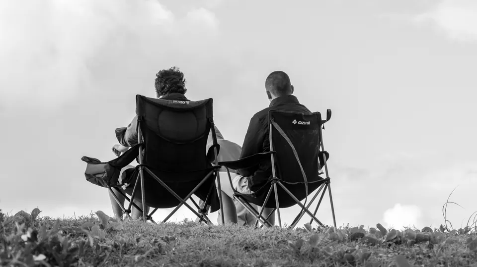 Black and white photograph of two people seated in camp chairs